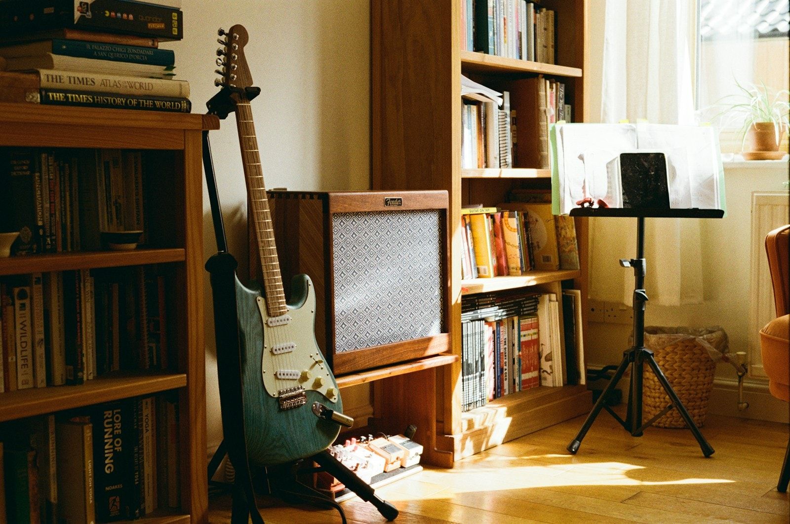 Canto de sala com estantes de livros, uma guitarra no suporte e uma estante de partitura perto da janela.