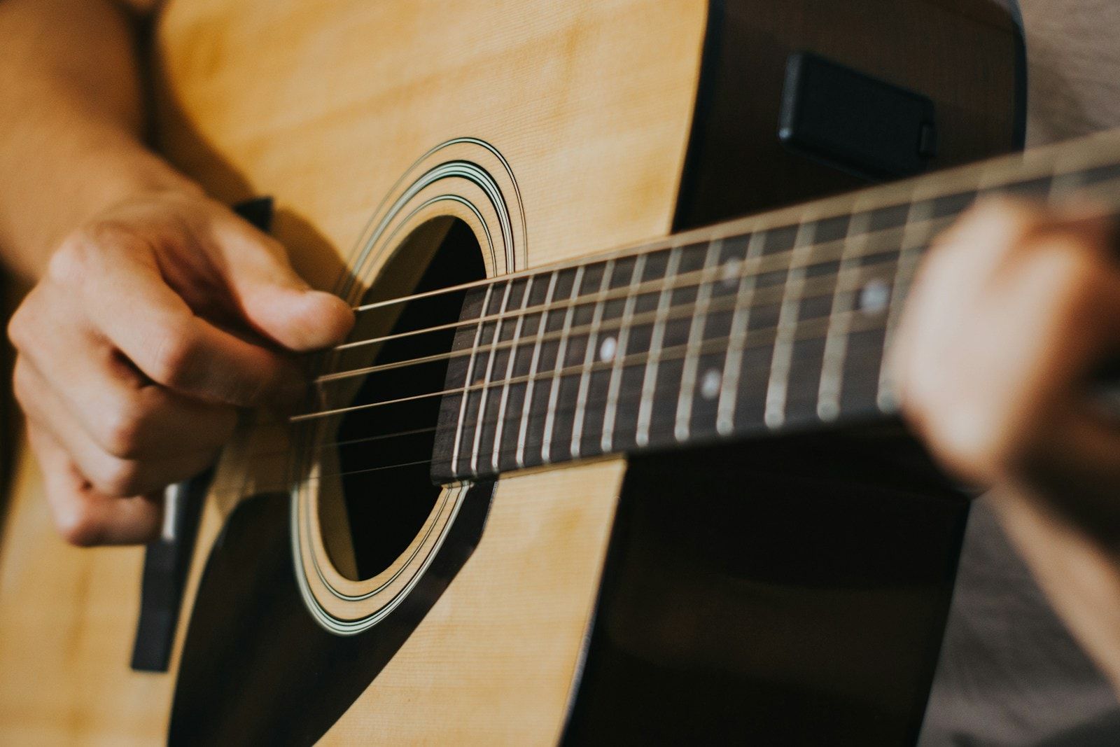 Close das mãos de uma pessoa tocando violão, uma dedilhando as cordas e a outra no braço do instrumento.