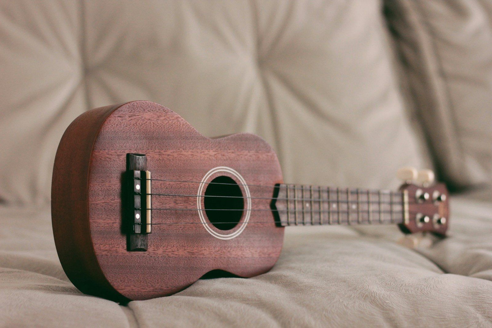 Ukulele de madeira escura deitado sobre uma almofada bege.